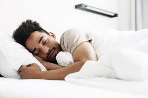 Photo of young african american man with mustache sleeping in white bed at bright room