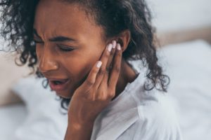 young african american woman suffering from ear or tooth pain in bedroom with closed eyes